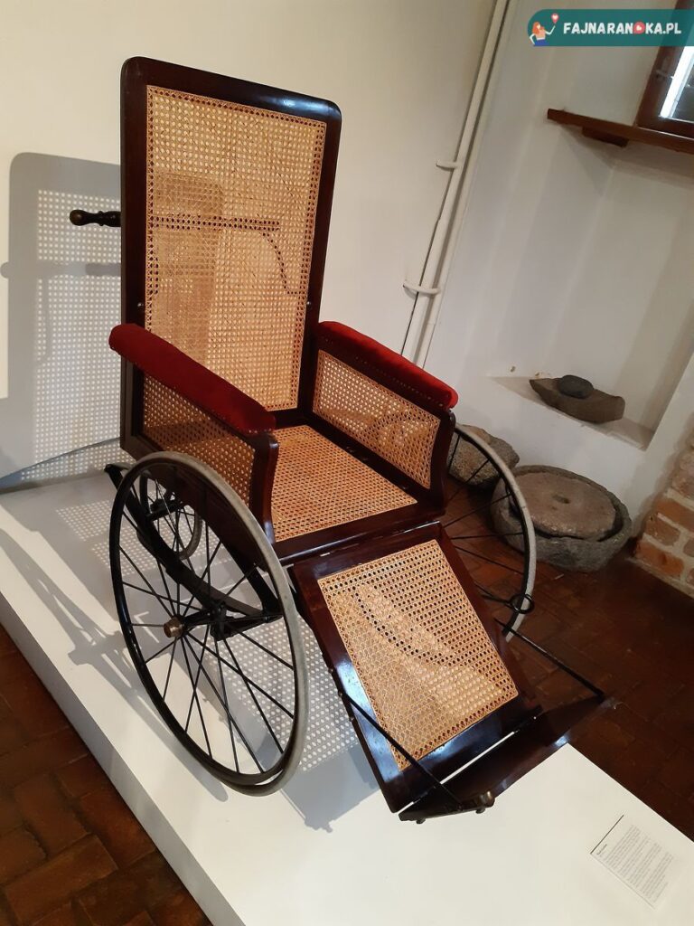 Stary, pleciony wózek inwalidzki w Szpitalu św. Ducha i Muzeum Medycyny we Fromborku.