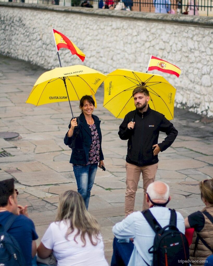 Para przewodników turystycznych z żółtymi parasolami,z firmy Walkative prowadzą spacer w języku hiszpańskim.
